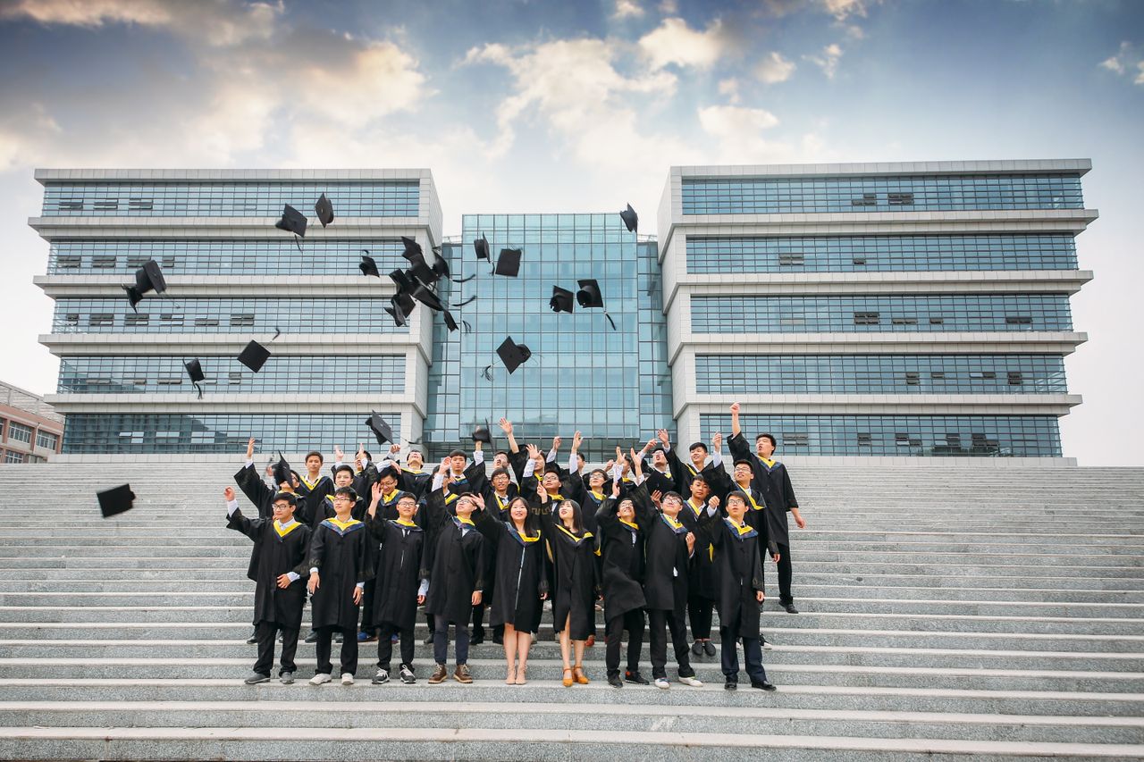 Group of graduates celebrating and tossing caps outside modern building.
